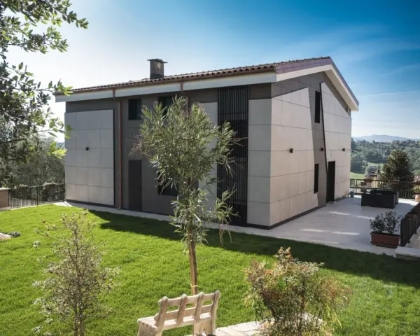 Esterno di case moderne con facciata in pannelli chiari e scuri, giardino curato e vista panoramica.