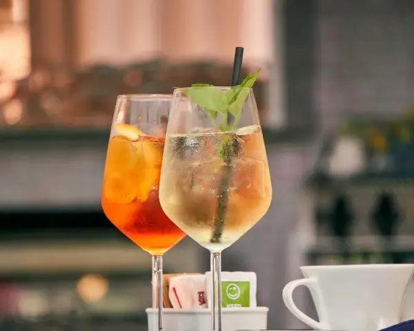 Dwa drinki w kieliszkach: pomarańczowy Aperol i jasny, z miętą. Aperol kontra Campari – wybór należy do Ciebie!