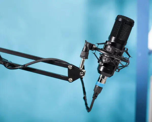Czarny mikrofon pojemnościowy na wysięgniku, gotowy do nagrania podcastu. W tle niebieskie tło.