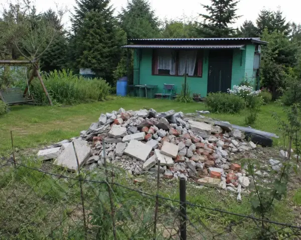 Kupa gruzu na działce ROD. Czy komornik może zająć działkę ROD? W tle zielona altanka, huśtawka i drzewa.