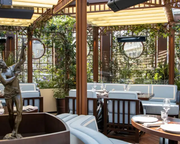 Terrazza lussuosa con statue e piante, tavoli apparecchiati per un'esperienza culinaria al **Wilde Milano**.