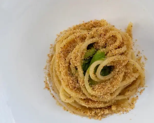 Spaghetti conditi con aglio, olio e peperoncino, cosparsi di pangrattato croccante e qualche foglia verde.