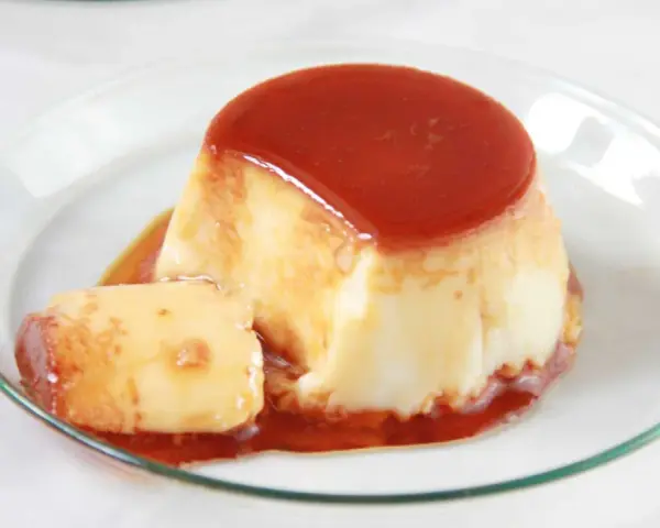 Delicioso flan de huevo en flanera con tapa, bañado en caramelo líquido y servido en un plato de cristal.
