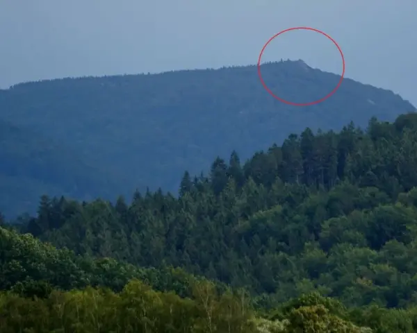 Górzyste krajobrazy czeskich Izery, z zalesionymi zboczami i skalistym szczytem zaznaczonym czerwoną obwódką.