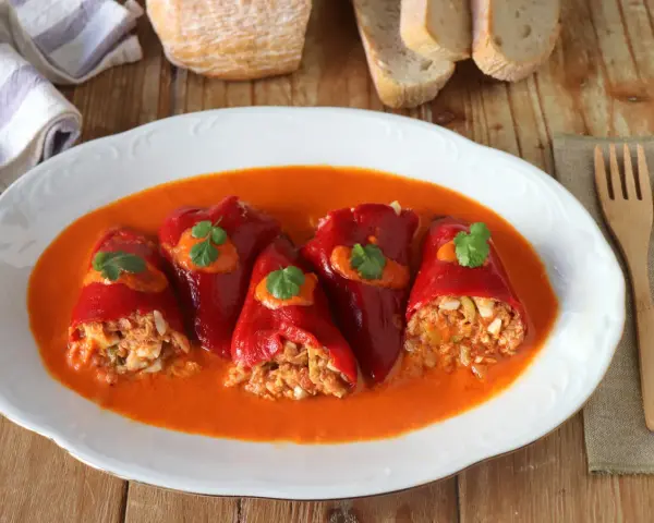 Pimientos del piquillo rellenos de atún y huevo, servidos en una salsa roja cremosa, decorados con perejil.