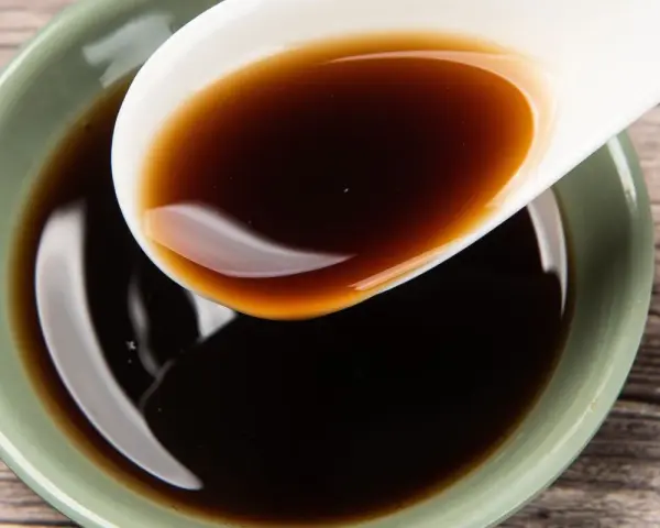 Łyżka z ciemnym, błyszczącym płynem, idealnym jako ocet balsamiczny do mięsa.