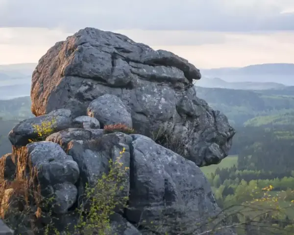 Skaliste formacje na tle zielonych gór w Czechach. Słońce oświetla skały, tworząc ciekawe cienie.