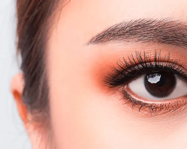 Occhi luminosi con un tocco di trucco coreano: ombretto pesca, eyeliner sottile e ciglia lunghe e folte.