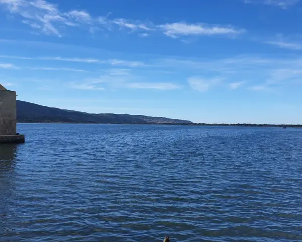 Mulino a Orbetello, un'icona da vedere. Paesaggio lagunare con cielo azzurro e colline sullo sfondo.