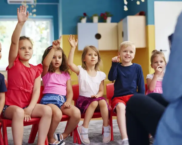 Dzieci na zerówce podnoszą ręce, chętne do odpowiedzi.