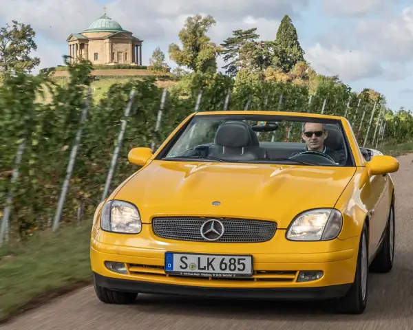 Gelber Mercedes SLK R170 Cabrio fährt durch Weinberge, im Hintergrund ein Tempel.