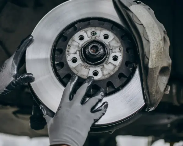 Mechanik w rękawiczkach wymienia zużyte tarcze hamulcowe. Widać nowy, lśniący element obok starego zacisku.