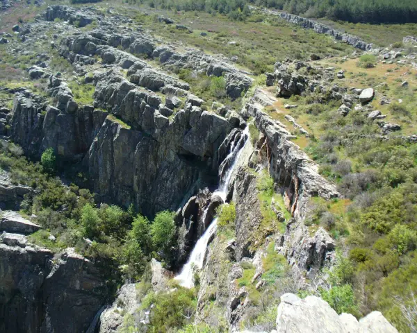 Cascada cayendo por rocas escarpadas cerca de un pico ocejon, rodeado de vegetación verde y rocas.