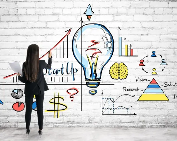 Mujer dibuja un gráfico de crecimiento y una bombilla, simbolizando cómo capitalizar el paro con una idea de startup.