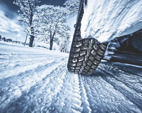 La gomma ghiaccio affronta la neve su una strada invernale, lasciando profonde tracce. Alberi innevati sullo sfondo.