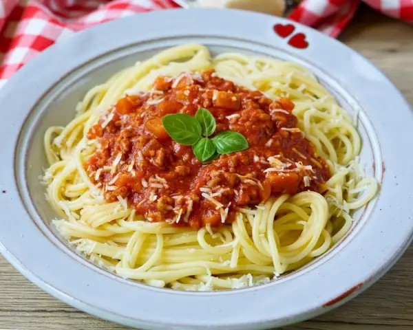 Teller mit Spaghetti Bolognese, bestreut mit Parmesan und garniert mit Basilikum. Perfekt für schnelle Bolognese für Kinder.