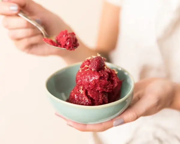 Ein Löffel Himbeersorbet-Rezept wird über eine Schüssel mit dem leuchtend roten Dessert gehalten, garniert mit einer Himbeere.
