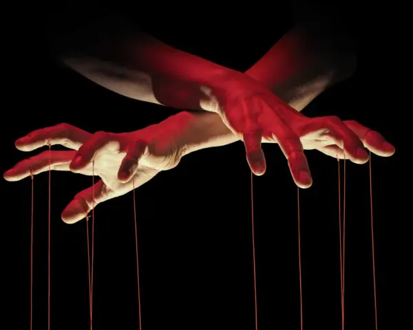 Dłonie jak marionetka, sterujące sznurkami. Czerwone światło podkreśla makiawelizm i manipulację.