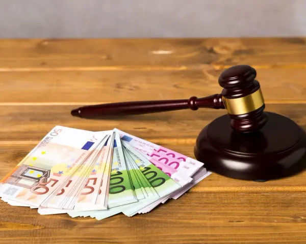 Ein Richterhammer liegt neben Euro-Scheinen. Die Frage "wie lange muss eine Rechtsschutzversicherung bestehen?" wird hier visuell thematisiert.