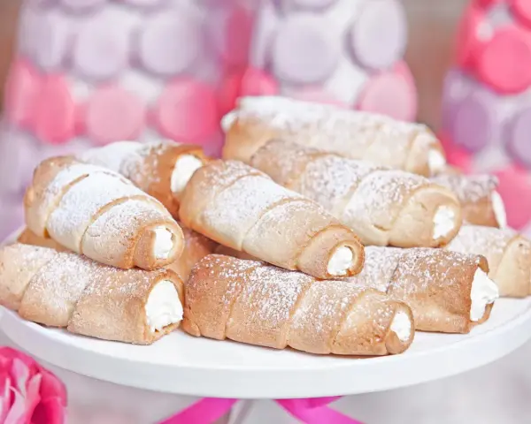 Domowe rurki z kremem, posypane cukrem pudrem, wyglądają apetycznie obok pastelowych dekoracji.
