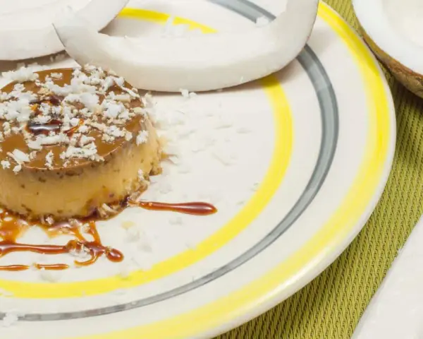 Flan coco on a plate, garnished with coconut flakes and caramel. A perfect dessert for your recette flan coco lait concentré Nestlé.