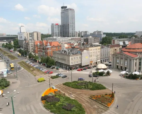 Widok na ruchliwy rynek w Katowicach z tramwajami, samochodami i budynkami.