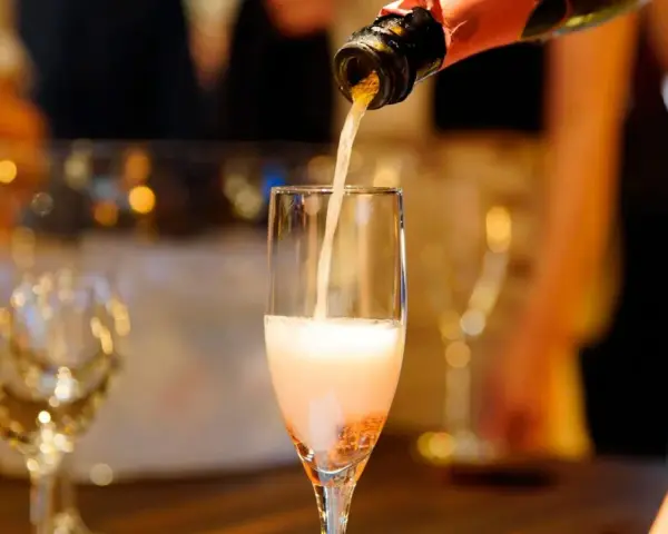Nalewanie musującego **cava wino** do kieliszka. W tle widać inne kieliszki i rozmyte światła, sugerujące uroczystą atmosferę.