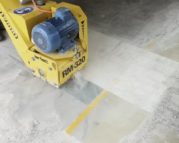 Żółta maszyna do szlifowania betonu RM-320 pracuje na posadzce, tworząc pył.