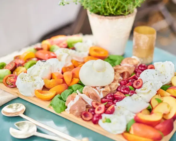 Eine bunte Antipasti Platte anrichten mit Burrata, Kirschen, Pfirsichen, Tomaten und Prosciutto.