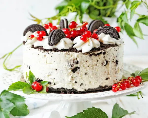 Pyszny tort z kawałkami oreo ciastka, udekorowany bitą śmietaną i czerwonymi porzeczkami.