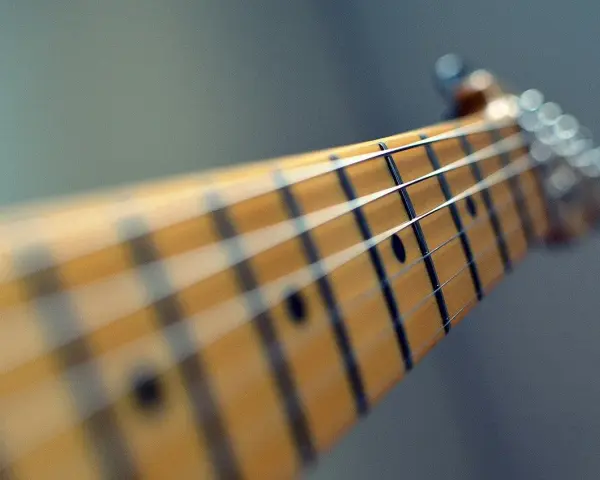 Zbliżenie na gryf gitary, gdzie ja gram na gitarze chwyty. Widać struny i progi.