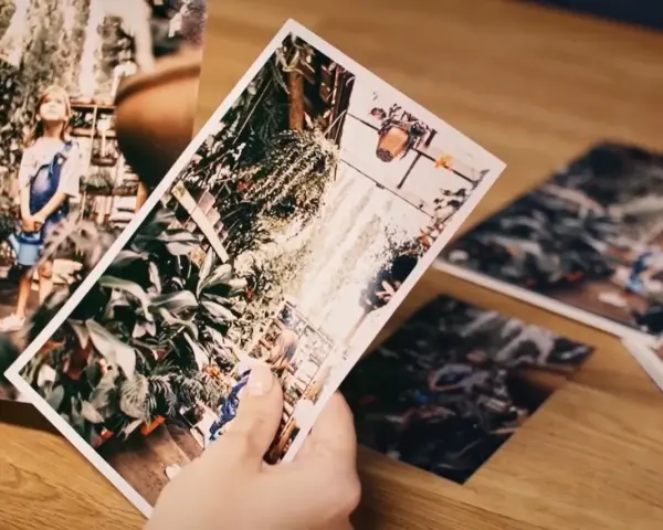 Dłonie trzymają zdjęcia, jedno z nich to dziewczynka z konewką, inne to rośliny. Jaki to format? 20x30.