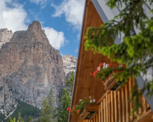 Drewniany domek z kwiatami w skrzynkach na tle skalistych Dolomitów.