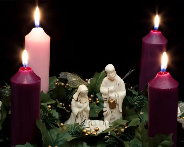 Three lit candles, two purple and one pink, surround a nativity scene. This is the advent 3rd Sunday.