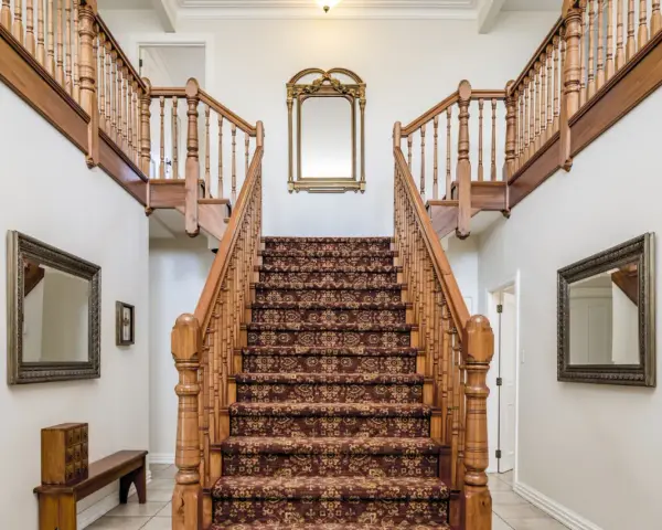 Elegante escalera antigua con alfombra de estilo persa y barandillas de madera. Un espejo dorado decora la pared central, complementando el revestir escalera antigua.