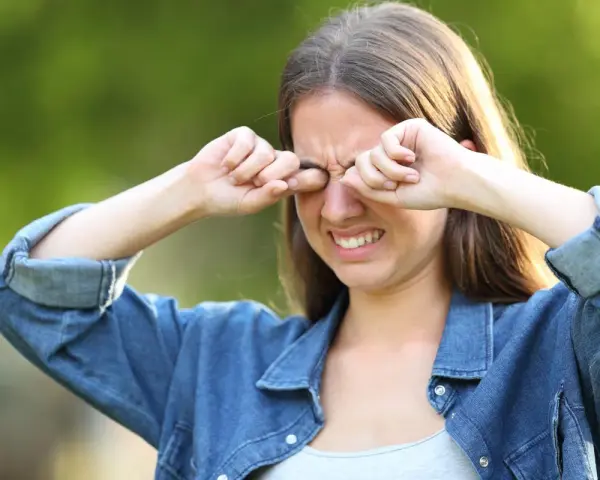 Ragazza con espressione infastidita, si stropiccia gli occhi con le mani, forse per il sole o per la stanchezza.