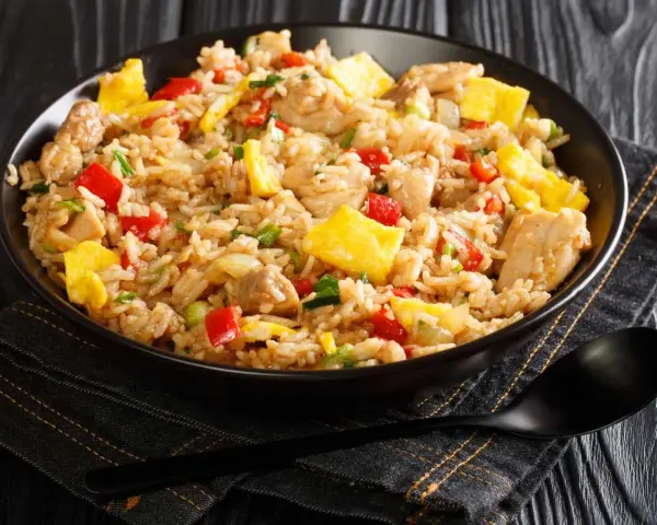 Un plato humeante de arroz chaufa con trozos de pollo, huevo revuelto, pimientos rojos y cebolla verde.