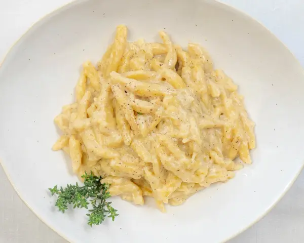 Ravioles val varaita, pasta fresca condita con una cremosa salsa al formaggio e pepe nero, guarnita con timo fresco.