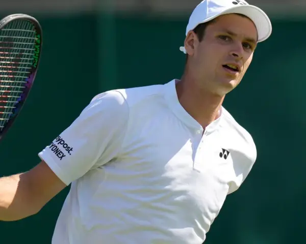 Hubert Hurkacz w białej koszulce i czapce, gotowy do uderzenia rakietą na Wimbledonie.