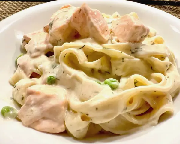 Cremige Nudeln mit Lachs, Erbsen und Dill in einer weißen Schüssel.