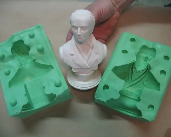 Making silicone molds for resin casting. A white bust is held between two green silicone molds, ready to capture its detail.