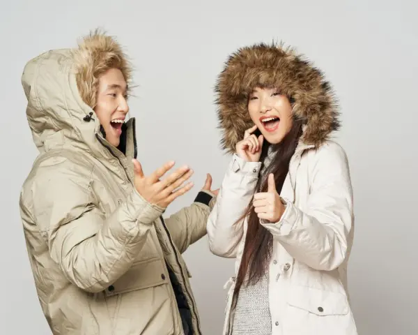 Pareja feliz con abrigos de invierno, ¡el mejor abrigo para el frío! Ella da pulgar arriba, él gesticula.
