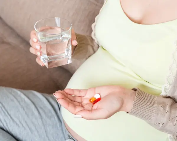 Kobieta w ciąży bierze suplementy, w tym magnez, popijając wodą. Dba o zdrowie swoje i dziecka.