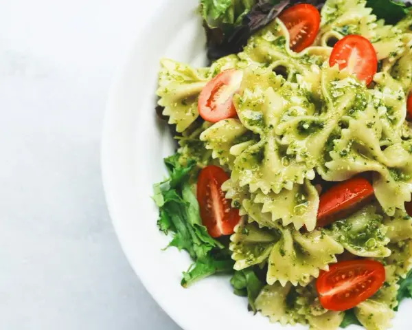 Pyszny makaron farfalle z aromatycznym pesto i soczystymi pomidorkami koktajlowymi, podany na liściach sałaty.