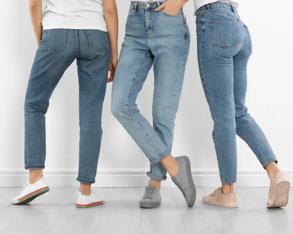 Trzy kobiety w jeansach i sneakersach. Dowiedz się, jak rozciągnąć jeansy, by były idealnie dopasowane.