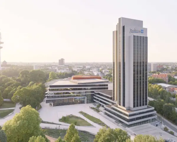 Radisson Blu Hotel w Hamburgu, z wieżą telewizyjną w tle, otoczony zielenią.