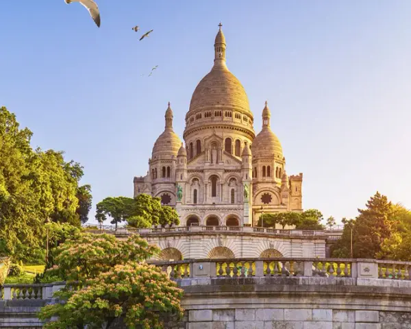 El barrio Montmartre, con la basílica del Sacré-Cœur al fondo, un carrusel y árboles frondosos bajo un cielo azul.