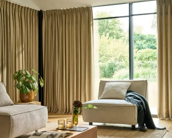 Salon moderne avec canapé beige, fauteuil, plante verte et rideaux au **type de pli rideau** qui habillent une grande baie vitrée.