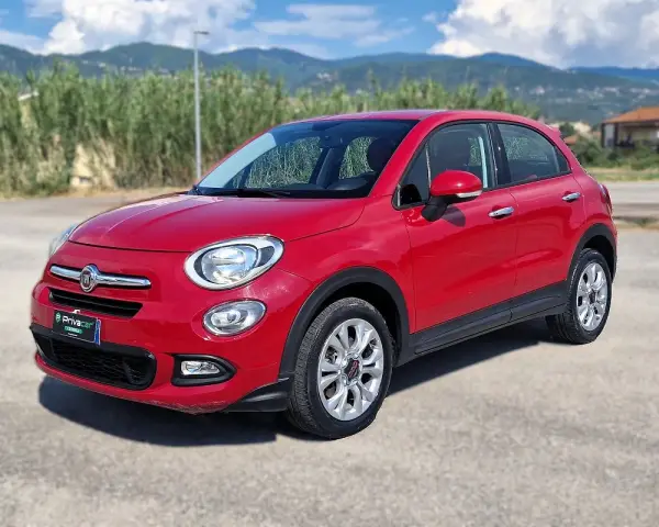 Fiat 500X rossa parcheggiata all'aperto, con montagne sullo sfondo. La pressione gomme è ottimale per ogni viaggio.