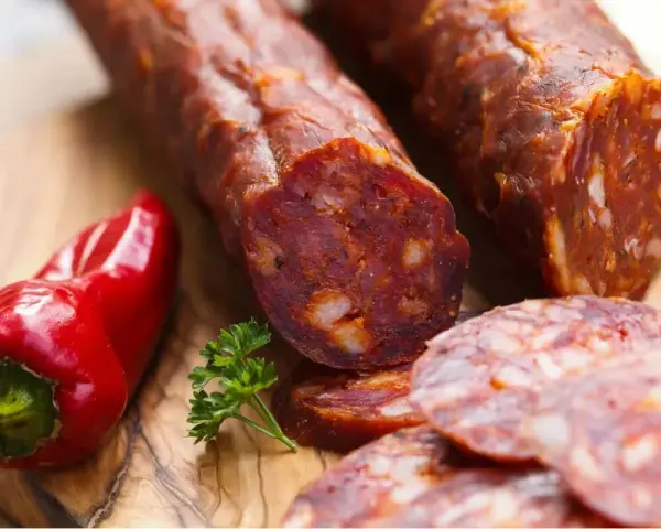 Kawałki pikantnego chorizo, czerwona papryczka i natka pietruszki na desce. Chorizo co to? To aromatyczna kiełbasa!